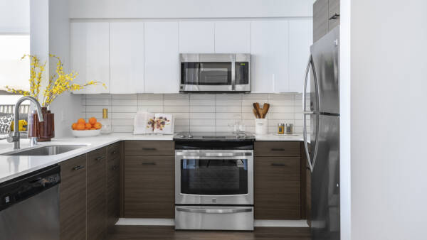 Apartment kitchen with stainless steel appliances, quartz countertops, and wood-style flooring.