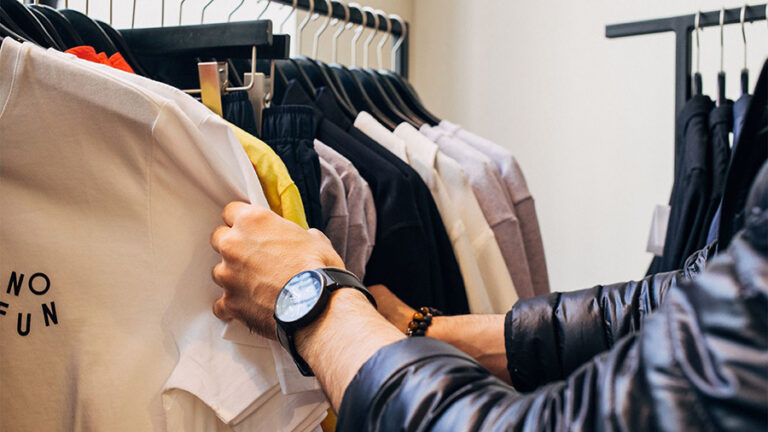 Person looking at shirts hanging on clothes rack.