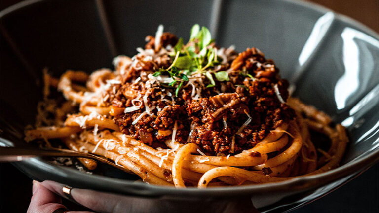 Person holding bowl of spaghetti with red meat sauce.