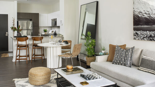 Apartment kitchen with stainless steel appliances, dining and living room with wood-style flooring.