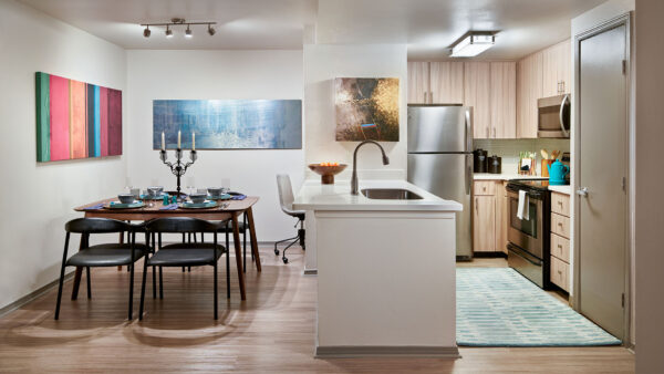 Apartment kitchen with stainless steel appliances, dining and living room with wood-style flooring.