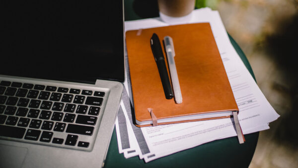 Desk with computer, papers, notebook, and pen.