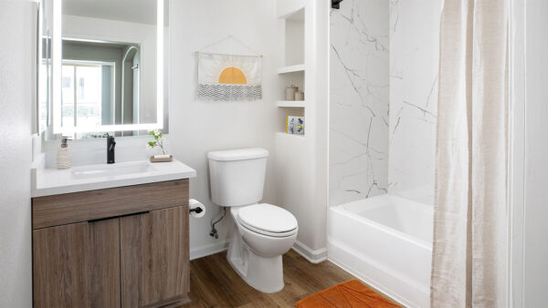 Apartment bathroom with wood-style flooring and LED vanity mirror.