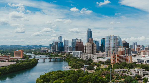 Austin skyline with tall glass buildings and tree lined river.