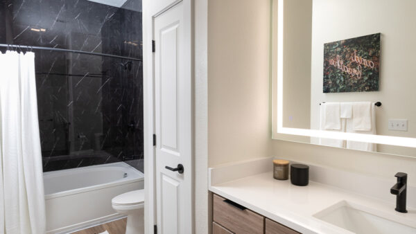 Apartment bathroom with wood-style flooring and LED vanity mirror.
