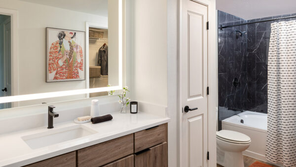 Apartment bathroom with large soaking tub, wood-style flooring and LED vanity mirror.