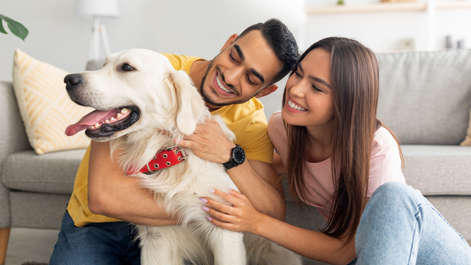 Resident couple smiling and holding holden retriever inside apartment home