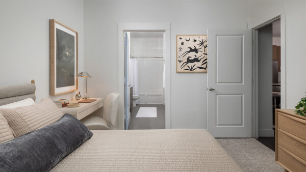 Spacious apartment bedroom with a large closet, attached bathroom, and plush carpet flooring.