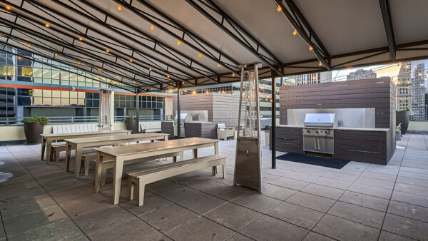 Luxury apartment outdoor grilling area with covered seating, communal dining table, and barbecue station