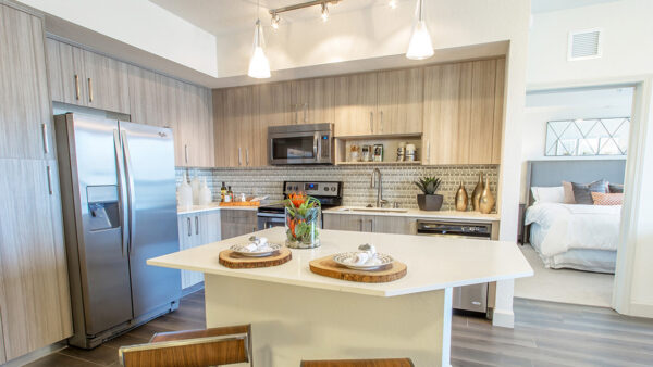 Open-concept luxury apartment kitchen with quartz island, stainless steel appliances, and wood cabinetry