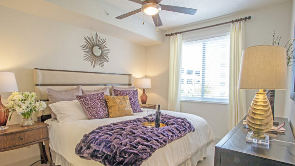 Luxury apartment bedroom with upholstered bed, ceiling fan, bedside lamps, and large window