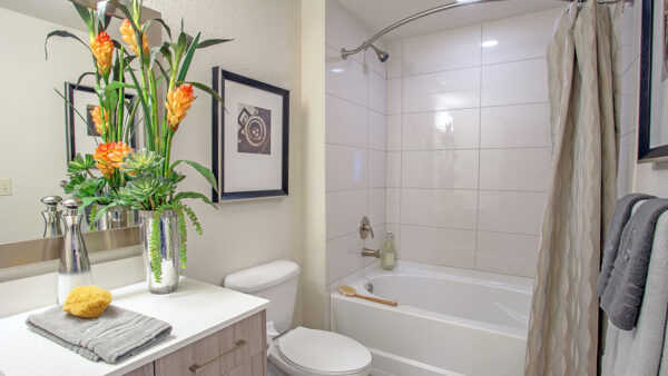 Luxury apartment bathroom with quartz vanity, soaking tub with tile surround, and modern fixtures