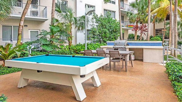 Luxury apartment outdoor amenity courtyard with pool table, grilling station, and landscaped seating area