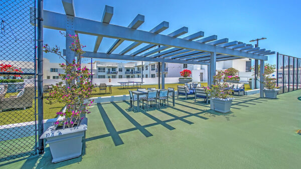 Luxury apartment rooftop lounge with pergola seating area, outdoor dining table, and city skyline views