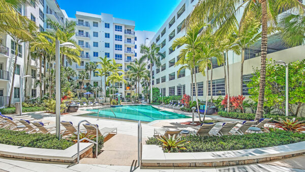 Luxury apartment resort-style pool with palm trees, sun loungers, and landscaped courtyard