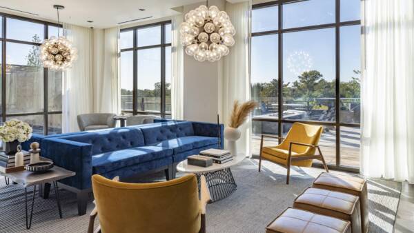 Griffis Edgemoor entertainment lounge with a blue velvet sofa, mustard chairs, and statement chandeliers.