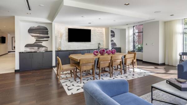 Griffis Edgemoor resident lounge with a dining table, blue sofa, and wall-mounted TV.