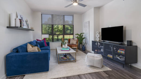 Griffis Edgemoor apartment living room with a blue sofa, TV console, and large windows.