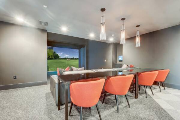 Griffis Platinum Triangle golf simulator lounge with orange chairs and a bar-height counter.